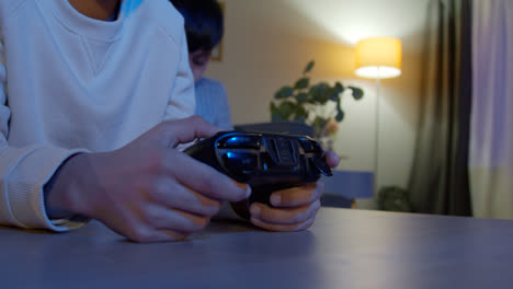 Close-Up-On-Hands-Of-Two-Young-Boys-At-Home-Playing-With-Computer-Games-Console-On-TV-Holding-Controllers-Late-At-Night